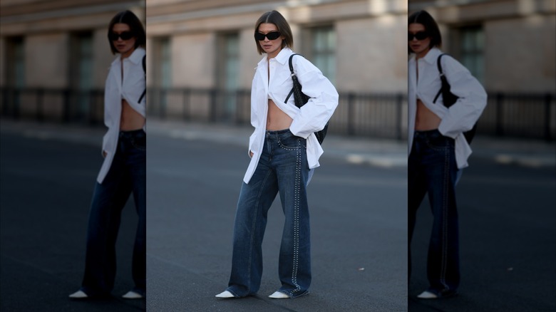 Une femme vêtue d'un jean foncé et d'un chemisier blanc.