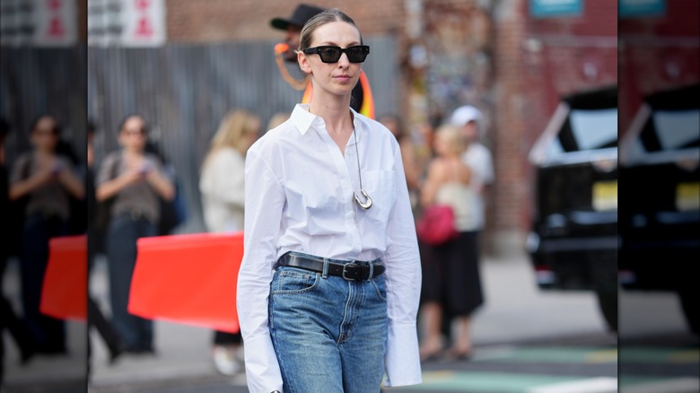Une femme vêtue d'une chemise blanche, d'un jean et d'un collier en argent avec un grand pendentif.