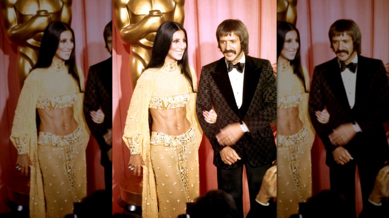 Cher portant un deux pièces doré scintillant posant bras dessus bras dessous avec Sonny Bono portant un smoking marron à motifs.