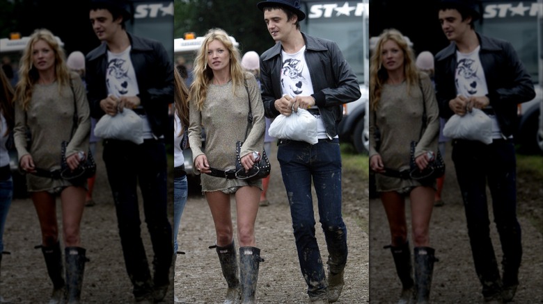 Kate Moss portant une tenue ébouriffée avec des bottes hautes et Pete Doherty portant un jean, une chemise blanche et un blouson aviateur noir, marchant dehors.