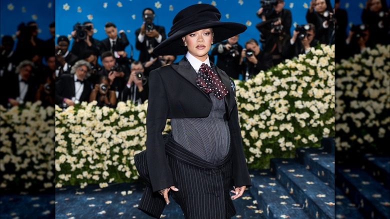 Rihanna posant au Met Gala 2025 portant une tenue inspirée de la mode masculine avec un nœud papillon souple et un grand chapeau noir.