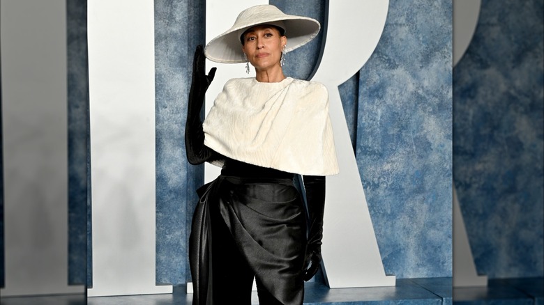 Tracee Ellis Ross posant lors d'un événement sur le tapis rouge, vêtue d'une tenue noire et de gants avec un caplet blanc et un chapeau blanc.