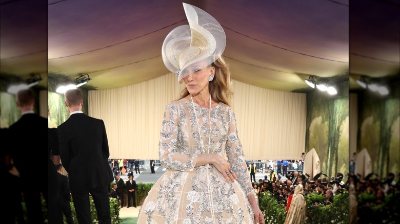 Sarah Jessica Parker posant au Met Gala 2024 portant une robe pêche et un chapeau orné.