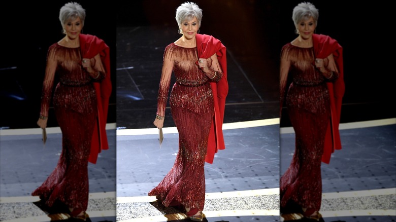 Jane Fonda posant aux Oscars vêtue d'une robe rouge pailletée avec un manteau rouge vif sur l'épaule.