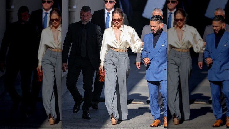 Jennifer Lopez photographiée à l'extérieur portant un pantalon large gris avec un haut blanc soyeux et des lunettes de soleil.