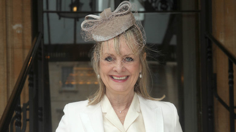 Twiggy porte un costume blanc et un chapeau fascinateur.
