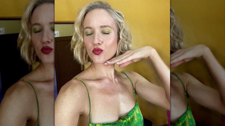 Jess Schram prend un selfie sur le plateau avec un fard à paupières vert et les lèvres plissées