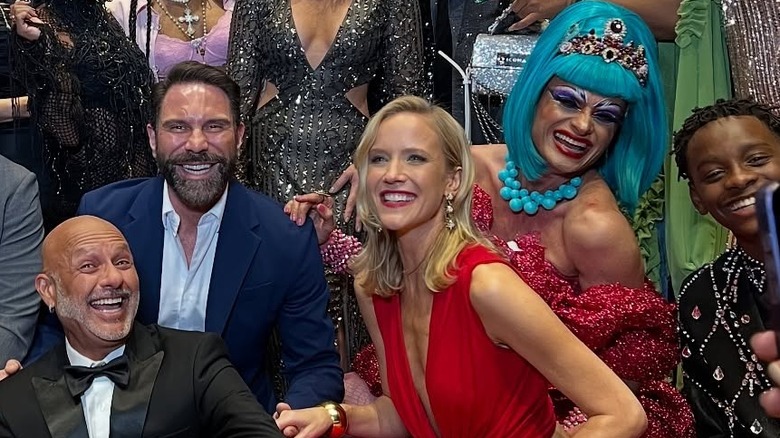 Jessy Schram pose avec un groupe de personnes portant des lèvres rouges et une robe rouge découpée