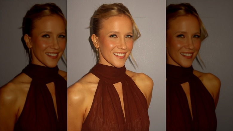 Jessy Schram souriante portant une robe marron et un chignon