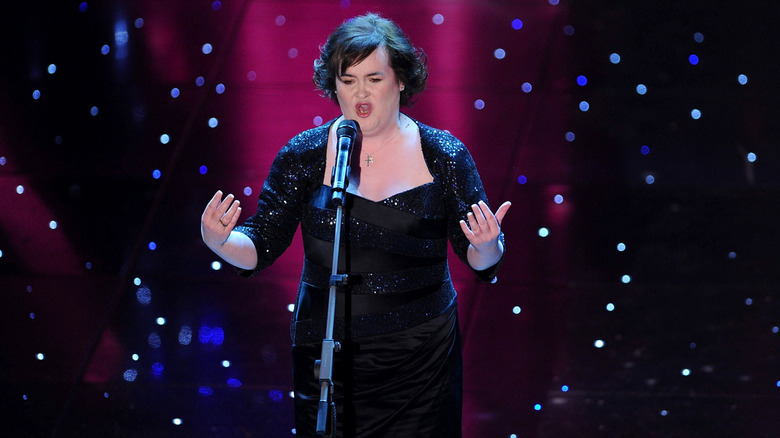 Susan Boyle chante dans un micro vêtue d'une robe noire à paillettes