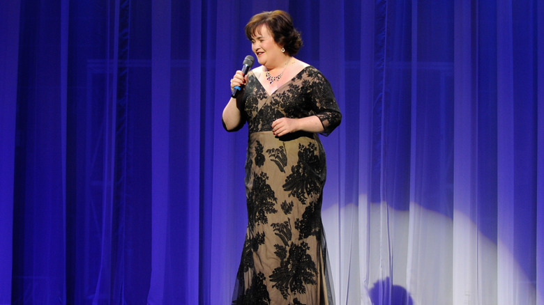 Susan Boyle tient un micro et porte une robe en dentelle noire