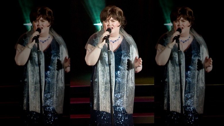 Susan Boyle chante dans un micro vêtue d'une robe bleue à paillettes