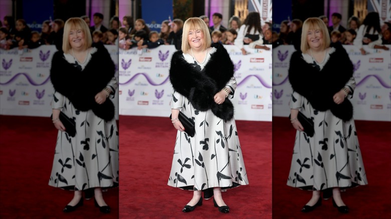Susan Boyle sourit en portant un boléro en fourrure noire et une robe noire et blanche