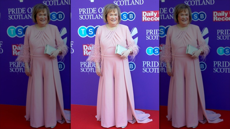 Susan Boyle sourit dans une robe rose avec des poignets en plumes