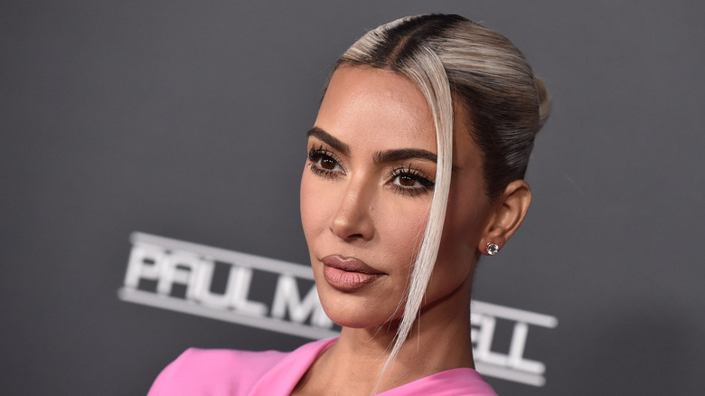 Kim Kardashian pose avec ses cheveux blonds plaqués en arrière et un haut rose