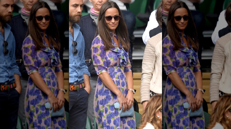 Pippa Middleton portant une robe à fleurs violette avec des lunettes de soleil tenant une pochette bleue à Wimbledon en 2016.
