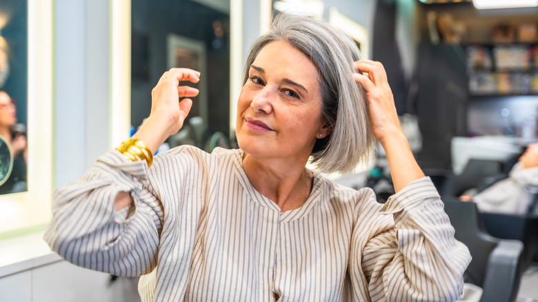 Une femme avec une coupe de cheveux grise jusqu'au menton touchant ses cheveux dans un salon.