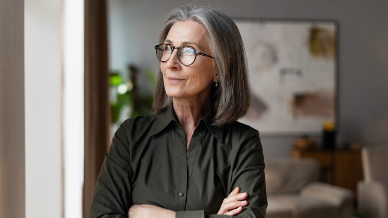 Une femme portant des lunettes avec une strie grise dans le lobe croisant les bras et regardant sur le côté.