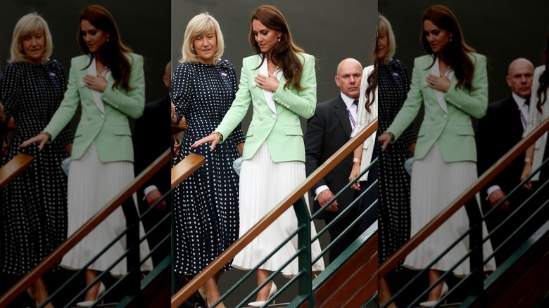 Kate Middleton descendant les escaliers portant une jupe plissée blanche et une veste vert clair avec bordure blanche à Wimbledon en 2023.
