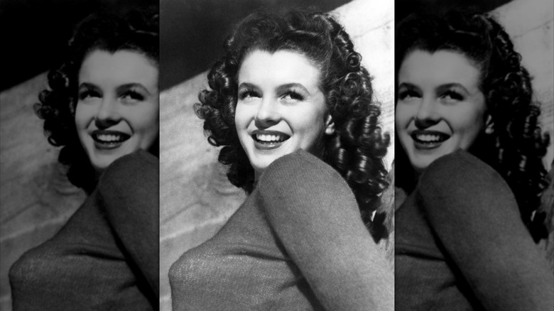 Photo en noir et blanc de Marilyn Monroe souriante et regardant par-dessus son épaule avec des cheveux bruns bouclés.