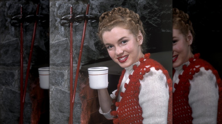 Marilyn Monroe posant en 1946, tenant une tasse avec ses cheveux tressés et portant un gilet en tricot rouge sur un pull blanc.