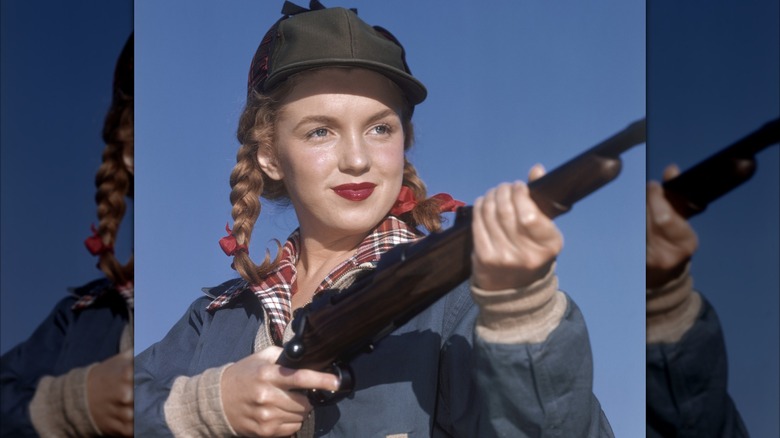 Marilyn Monroe posant en 1946 tenant un fusil, portant une chemise à carreaux, un chapeau de chasse et un rouge à lèvres avec ses cheveux tressés.