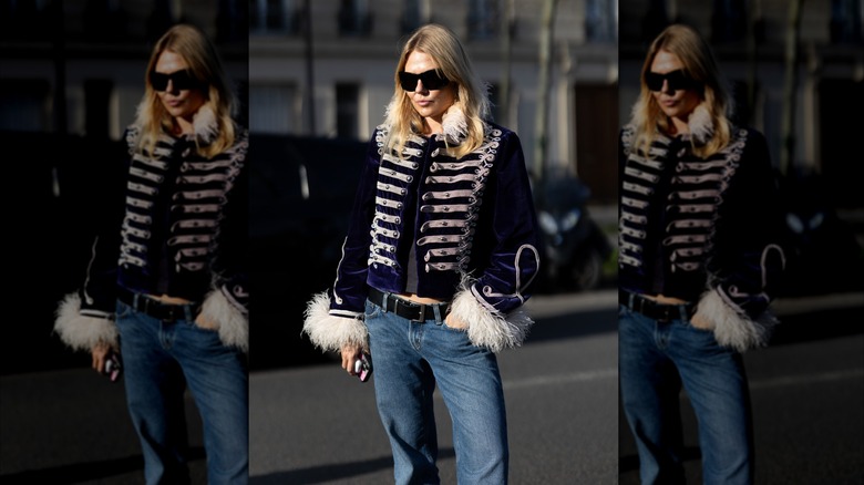 Une femme portant un manteau de style militaire avec des manches et un col en fourrure avec un jean et une ceinture noire.