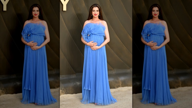 Anne Hathaway pose ses mains sur son ventre dans une robe bleue