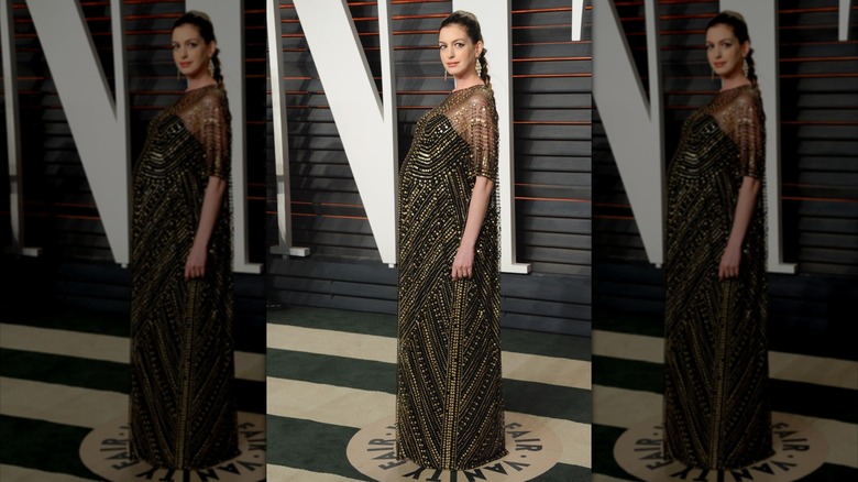 Anne Hathaway pose dans une robe noire et dorée qui met en valeur son baby bump