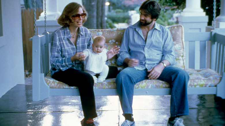 Cybill Shepherd sur une balançoire, vêtue d'une chemise bleue et tenant sa petite fille à côté de David M. Ford.