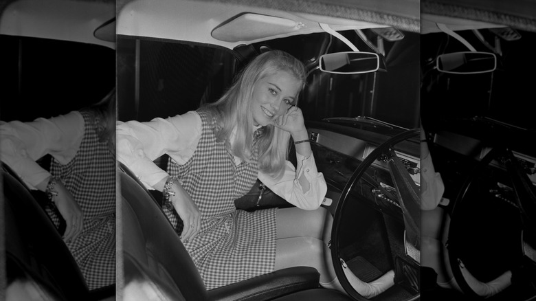 Une photo en noir et blanc de Cybill Shepherd assise dans une voiture et vêtue d'une robe à carreaux.