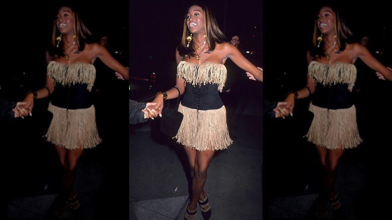 Naomi Campbell porte une robe à franges noire et beige.