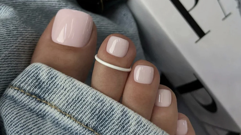 Pédicure rose pâle avec un anneau d'orteil blanc sur le deuxième orteil