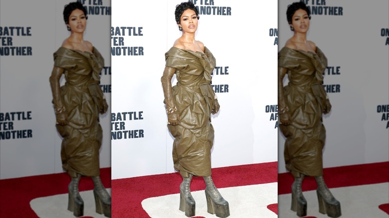 Teyana Taylor posant sur un tapis rouge vêtue d'une robe en cuir olive avec des bottes à plateforme.
