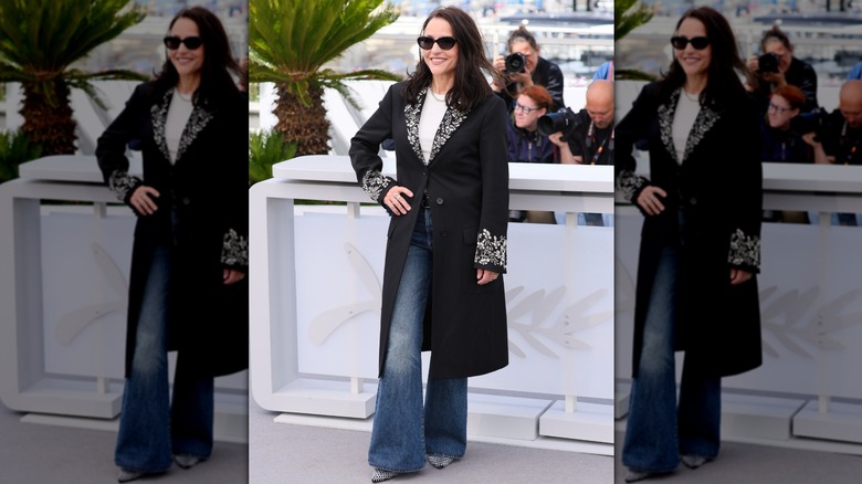 Julia Louis-Dreyfus posant lors d'un événement avec la main sur la hanche, portant un jean évasé, un manteau noir et des lunettes de soleil foncées.