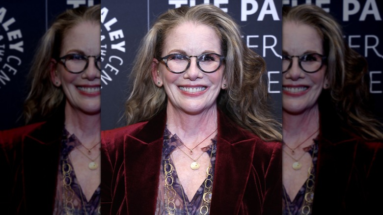 Melissa Gilbert sourit avec des lunettes rondes et un blazer en velours rouge