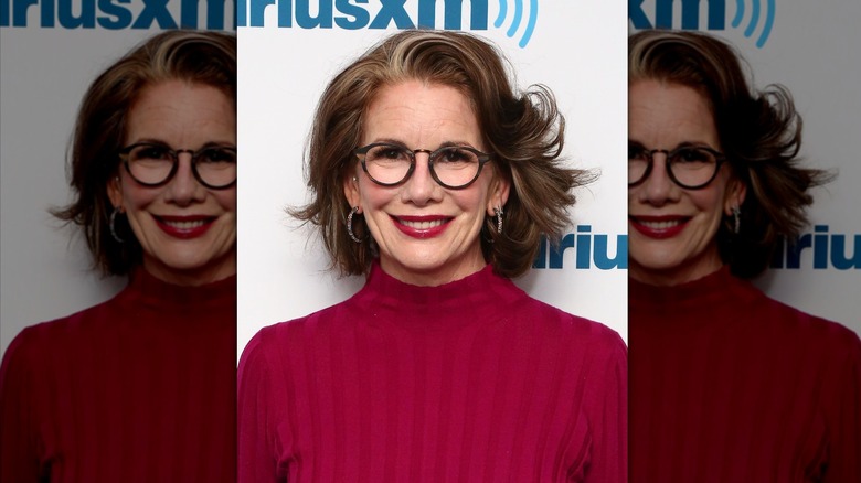 Melissa Gilbert sourit avec un col roulé rouge et des lunettes rondes