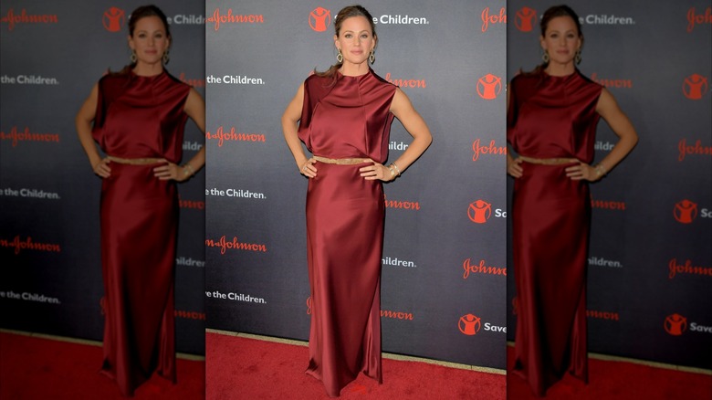 Jennifer Garner posant sur un tapis rouge vêtue d'une robe en satin rouge rubis avec une ceinture beige.
