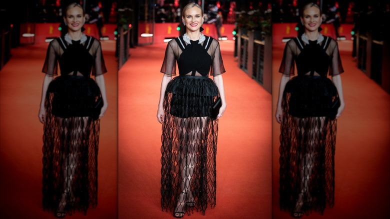 Diane Kruger sur le tapis rouge vêtue d'une robe noire à manches transparentes et d'un short noir recouvert d'une longue jupe en dentelle noire.