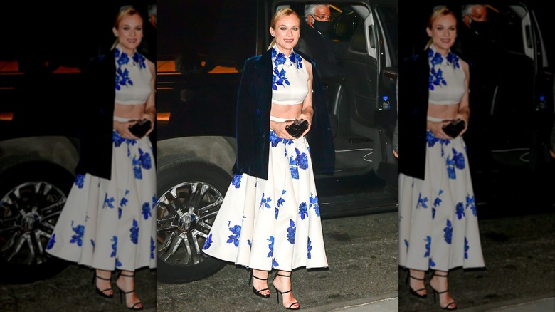 Diane Kruger lors d'un événement portant un ensemble haut court et jupe deux pièces à fleurs blanc et bleu avec une veste en velours bleu foncé.