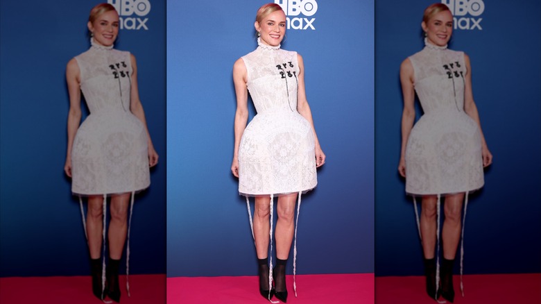Diane Kruger sur le tapis rouge vêtue d'une robe courte en dentelle blanche avec des bottes noires.