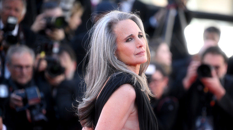 Andie MacDowell sur le tapis rouge vêtue d'une robe noire avec de longs cheveux gris.