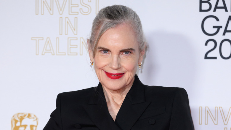Elizabeth McGovern lors d'un événement sur le tapis rouge, vêtue d'un haut noir avec un rouge à lèvres rouge vif et des cheveux gris coiffés d'un chignon.