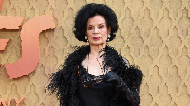 Bianca Jagger porte une robe noire et une veste à plumes.