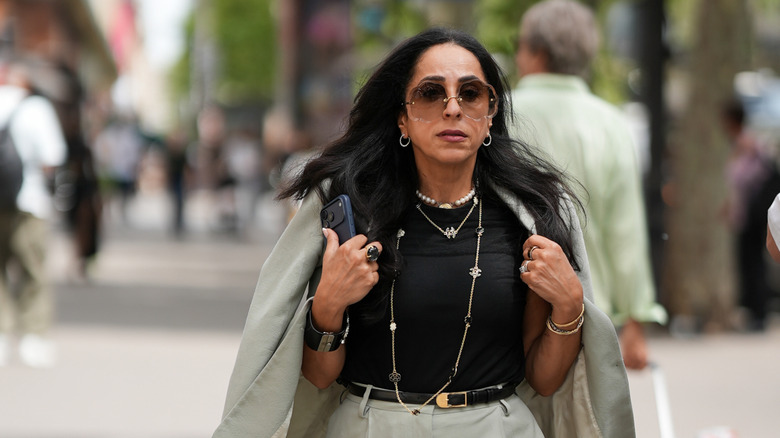Une femme porte un blazer, un t-shirt noir et un collier tendance