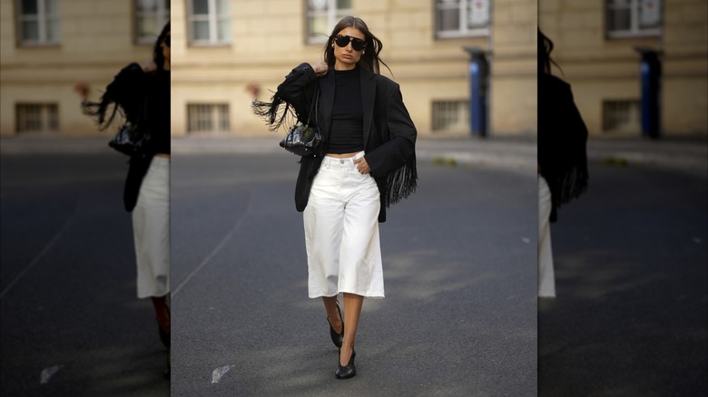 Une femme portant un blazer à franges noir et une jupe-culotte large blanche.