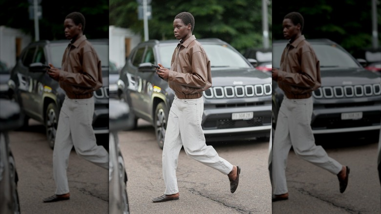 Une femme portant des mocassins noirs, un jean blanc et un blouson aviateur marron.