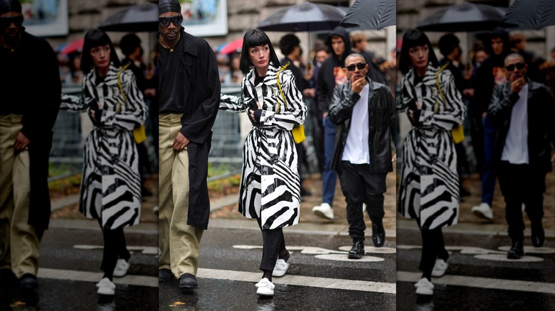 Une femme lors de la Fashion Week de Paris 2024 porte un imperméable rayé noir et blanc avec des mocassins à enfiler blancs.