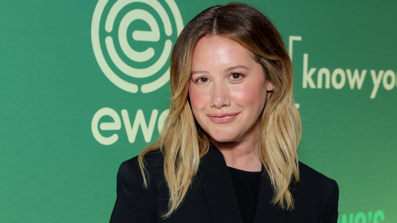 Ashley Tisdale dans un blazer noir, souriante, les cheveux détachés.