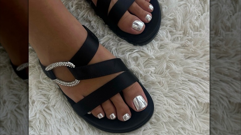 Gros plan des pieds d'une femme avec une pédicure chromée argentée, portant des sandales noires